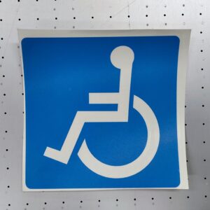 Blått kvadratisk klistremerke med hvitt universelt symbol for rullestolbrukere, vist på en lys bakgrunn